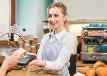 Vendedora atrás de um balcão em uma loja segura uma máquina de cartões para que cliente digite a senha.