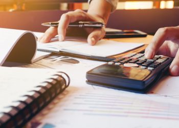 Homem mexendo na calculadora e fazendo anotações com caneta.