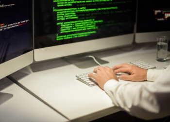 Imagem de uma mão masculina programando em telas de computadores