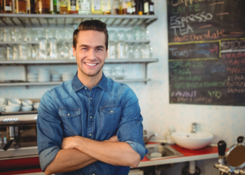 Homem olha para câmera em sua loja sorrindo.