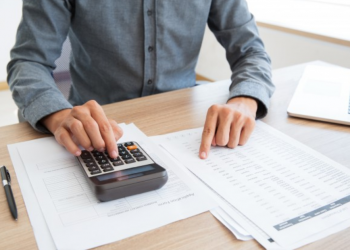 Homem analisa uma lista com uma mão e na outra faz contas em uma calculadora