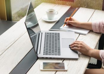 Mulher trabalhando em seu computador e fazendo anotações em um papel