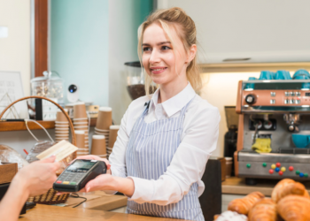 Imagem de uma atendente de café entregando maquininha para cliente passar seu cartão